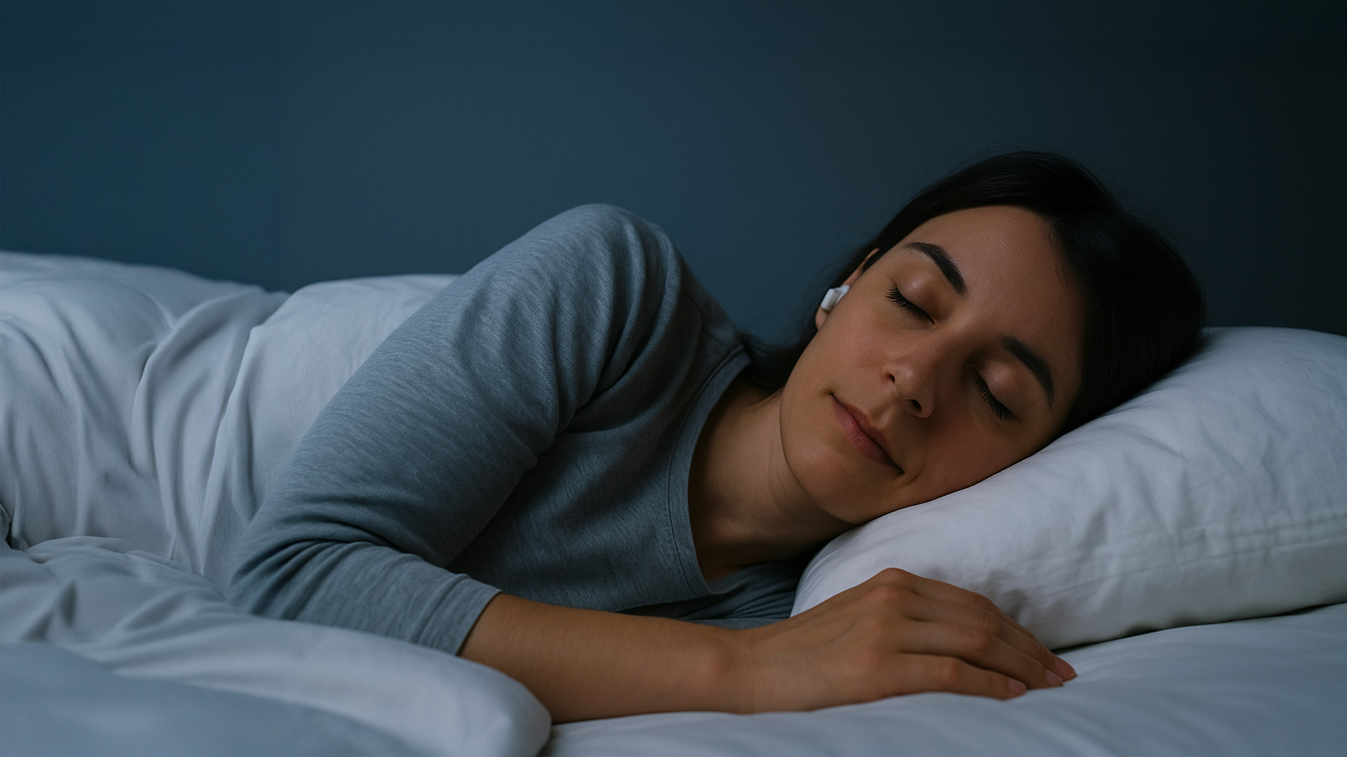 Kvinne som ligger på siden med ørepropper, rolig ansiktsuttrykk og lukkede øyne, i et dempet og behagelig miljø, illustrerer stillhet og god søvn.